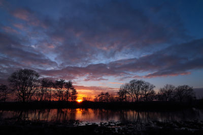 Silhouette trees by lake against sky during sunset