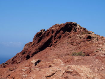 Low angle view of rocky mountain against clear blue sky