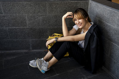 Portrait of smiling businesswoman sitting by wall