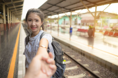 Portrait of smiling woman holding hands at railroad station platform