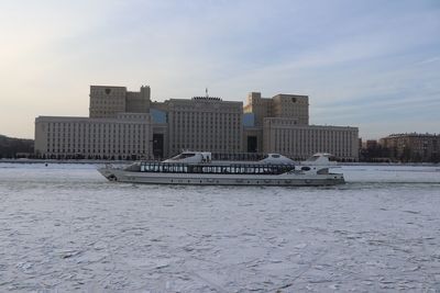 Buildings by frozen river against sky in city during winter