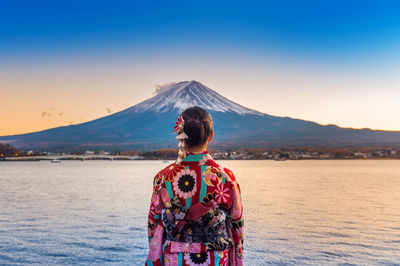 Woman standing by lake against sky during sunset