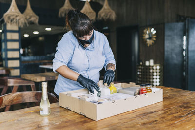 Female chef talking on phone while arranging take out box at kitchen counter in restaurant during pandemic