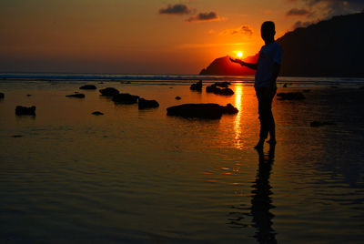 Silhouette man standing on beach against sky during sunset