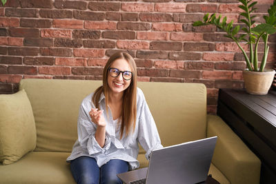 Portrait of young woman using laptop while sitting against wall