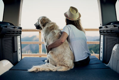 Unrecognizable female tourist embracing obedient golden retriever dog lying on mattress inside camper and admiring nature