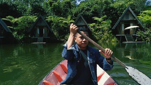 Portrait of young man rowing boat on lake against trees