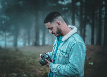 Side view of young man holding camera while standing on land