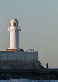 Lighthouse by sea against clear sky