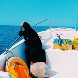 Rear view of woman in burka sitting on boat against sea