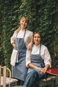 Portrait of smiling female chefs against plants at restaurant