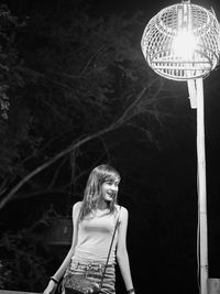 Smiling woman standing by illuminated street light at night