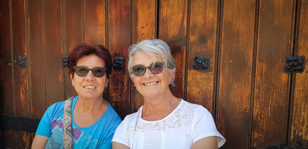 Portrait of smiling friends wearing sunglasses against closed wooden doors