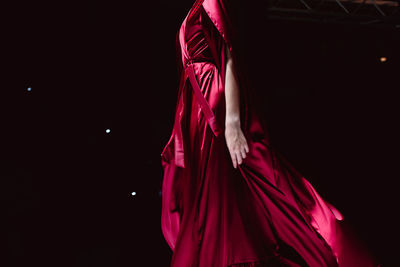 Elegant fashion details of red long silky dress. fashion model walking on black background