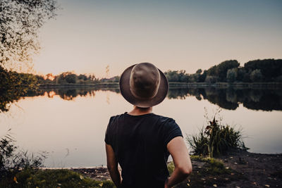 Rear view of young woman looking at lake against sky during sunset