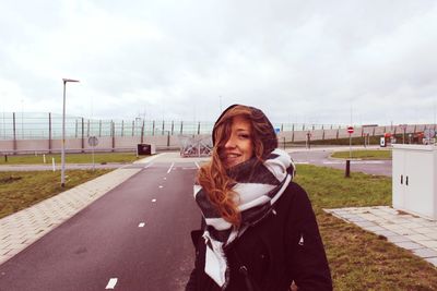 Portrait of smiling young woman wearing warm clothing while standing on road