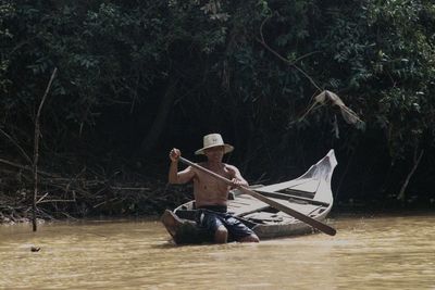 Man sitting on boat against trees