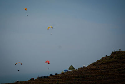 Low angle view of people paragliding against sky