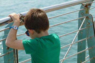 Rear view of boy standing by railing against sea