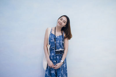 Portrait of smiling young woman standing against wall