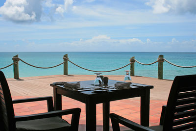 Empty chairs and table by sea against sky