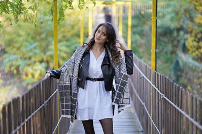 Portrait of young woman standing against railing
