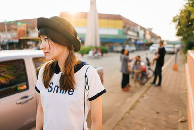 Young woman looking away while standing on sidewalk