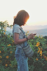 Young woman standing amidst flowering plants against sky