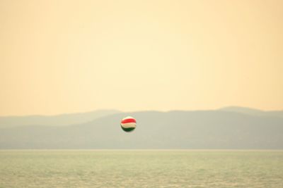Red balloons flying over sea against sky during sunset