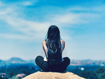 Rear view of woman sitting on rock against sky