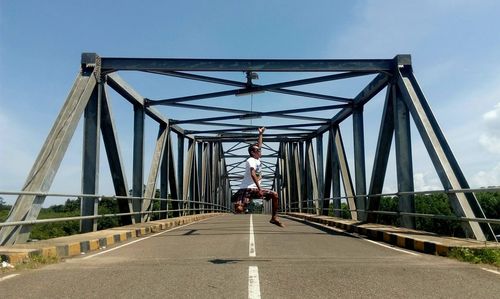 Rear view of woman walking on footbridge against sky