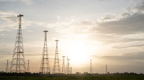 Low angle view of electricity pylon on field against sky during sunset