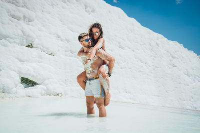 Full length of shirtless man with woman standing in water