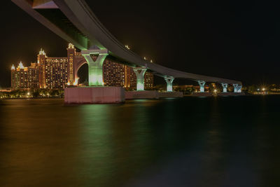 Illuminated bridge over river against sky at night