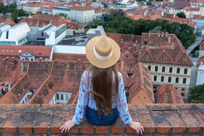 Rear view of woman sitting against buildings in city