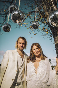Portrait of newlywed mid adult groom and bride standing under disco balls on sunny day