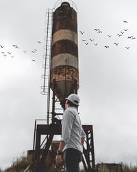 Rear view of man looking at birds against sky