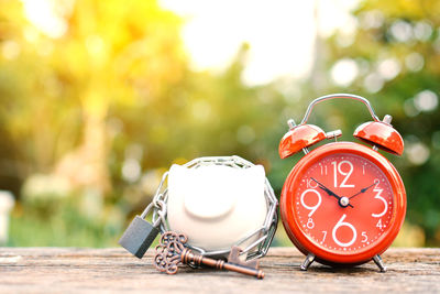 Close-up of red alarm clock with piggy bank on wooden table