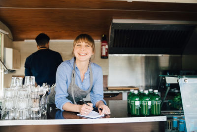 Portrait of happy female owner standing in food truck while coworker working in background