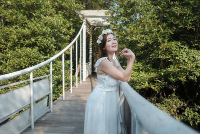 Portrait of bride standing by railing on footbridge in forest