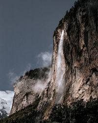 Low angle view of rock formation and waterfall against sky