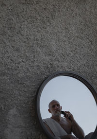 Shirtless adult man shaving himself with shaver in mirror