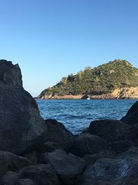 Scenic view of rocks by sea against clear blue sky