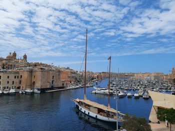 Sailboats moored in harbor by buildings in city against sky