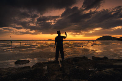 Silhouette man standing on beach against sky during sunset