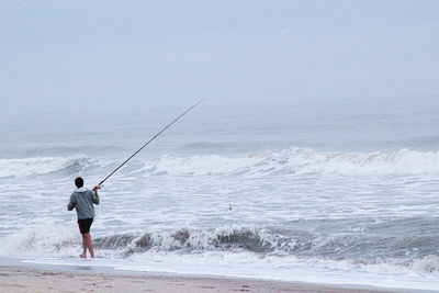 Rear view of man fishing in sea against sky