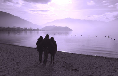 Rear view of female friends standing at beach against sky