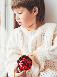 Kid with red decorative ball for christmas tree. boy in cable-knit oversized sweater. new year.