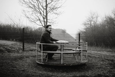 Man sitting on playground against trees