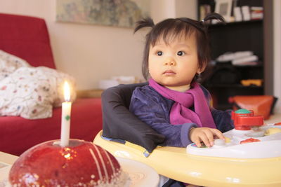 Cute girl sitting in baby walker by cake